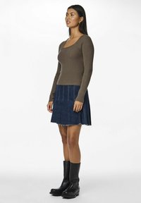 Brązowa, prążkowana bluzka z długim rękawem połączona z ciemnoniebieską spódnicą dzwonową z surowym wykończeniem i jasnym przeszyciem, noszona z czarnymi botkami na obcasie.