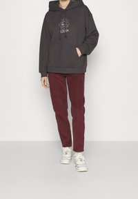 Felpa grigia scura con una grafica floreale colorata sul petto, abbinata a pantaloni in velluto a coste bordeaux e sneakers bianche. Design semplice.