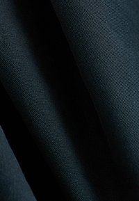 Dunkel gestrickter Stoff mit einem gewebten Muster, das mehrere Falten zeigt, die seine Dicke und matte Oberfläche betonen.