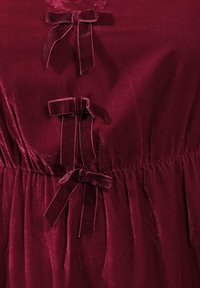Burgundy samettimekko, jossa on kolme koristeellista nauhaa, kerääntynyttä kangasta vyötäröllä ja sileä, kiiltävä pinta.