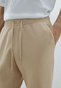 Beige joggerbroeken hebben een verstelbare tailleband, zijzakken, een soepel stoffen textuur en metalen accenten bij de koorden.