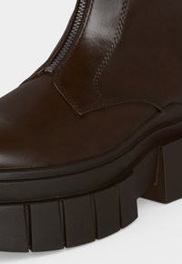 Κοντινή λήψη ενός σκούρου καφέ δερμάτινου μπότε που έχει χοντρή μαύρη σόλα με βαθιά σχέδια και εμφανές πλαϊνό φερμουάρ στο πάνω μέρος.