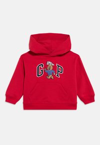 Κόκκινο παιδικό φούτερ με κουκούλα και μπροστινή τσέπη που απεικονίζει μια αρκούδα που περπατά κρατώντας μια σημαία και το κείμενο "GAP" σε ναυτικό μπλε και άσπρα γράμματα.
