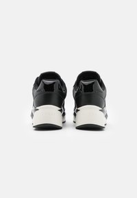 Svarta sneakers med glänsande och matta texturer, som har en tjock vit sula och varumärke på baksidan. Rundad form med vadderad krage.