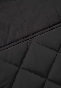 Sort quiltet stof med en glat tekstur. Har skrå sømme og diamantformede mønstre, hvilket viser et moderne design.