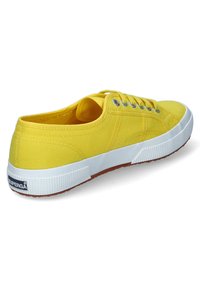 Sneaker di tela gialla con punta rotonda, suola in gomma bianca e occhielli in argento. Presenta una tomaia strutturata e un dettaglio del logo sul retro.