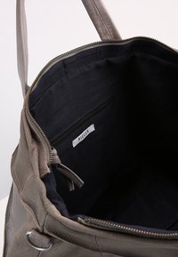 Sac à main en cuir taupe ouvert avec un intérieur en tissu noir, une poche intérieure zippée étiquetée "Pièces" et des tirettes en cuir sur la fermeture éclair.