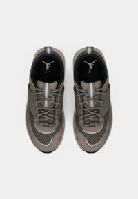 Beige und graue Sneaker mit Netz- und Wildlederpaneelen. Sie verfügen über ein schwarzes Innenfutter, reflektierende Akzente und ein auffälliges Logo auf der Zunge.