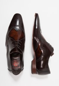 Chaussures habillées en cuir marron foncé avec une finition brillante, présentant des détails décoratifs perforés de style brogue, un bout pointu et un talon en bois.