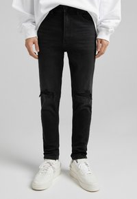 Svarta skinny jeans med rivna knädetaljer, tillverkade av denim, kombinerade med vita sneakers med en texturerad sula och snörning.