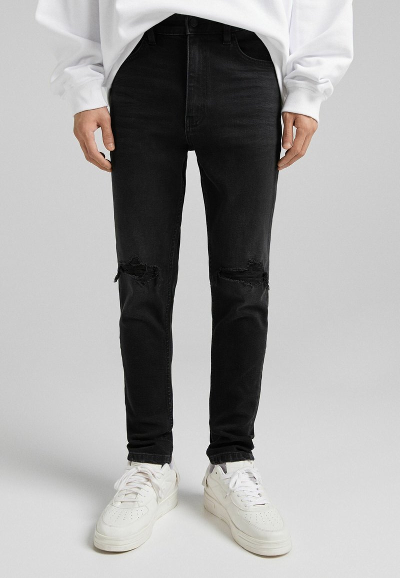 Svarta skinny jeans med rivna knädetaljer, tillverkade av denim, kombinerade med vita sneakers med en texturerad sula och snörning.