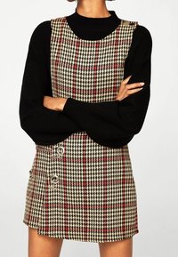 Ruudullinen minimekko beige, musta ja punainen sävyssä. Ominaisuudet neliömäinen kaula-aukko ja kaksi hopeista metallipainiketta sivussa. Teksturoitu kangas.
