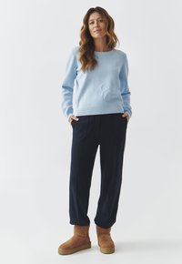 Pull en bleu clair avec des détails texturés, pantalon marine et bottines beige à la cheville. L'ensemble a une coupe décontractée et des poignets côtelés.