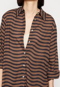 Camicia a righe marrone e blu navy, con chiusura a bottoni e maniche arrotolate. Realizzata in tessuto morbido con una texture fluida.