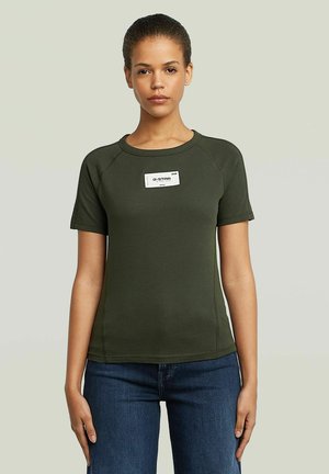 T-shirt vert olive à manches courtes avec un col rond, doté d'une étiquette blanche sur la poitrine, et d'une coupe ajustée avec des coutures latérales.