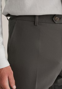 Sive prirejene hlače z gladko teksturo, z gumbom za zapiranje, stranskimi žepi in obročki za pas, v kombinaciji z svetlo obarvano srajco.