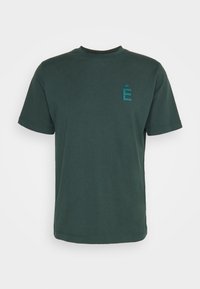 Tmavě zelené bavlněné tričko s kulatým výstřihem, krátkými rukávy a malým, tyrkysovým vyšitým písmenem "É" na hrudi.
