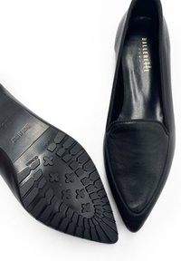 Bailarinas de cuero negro con un diseño de punta afilada, bordes elastizados y una suela de goma texturizada con un patrón antideslizante.