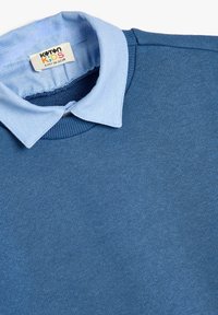 Suéter azul con un cuello tipo polo en un tono azul claro. Hecho de una tela suave, presenta una textura lisa y detalles acanalados a lo largo del cuello.
