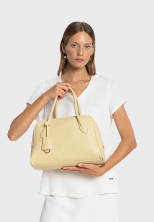 Sac à main en cuir jaune à forme arrondie, avec des poignées supérieures et une petite étiquette de bagage. Présente une surface texturée et un logo embossé sur le devant.