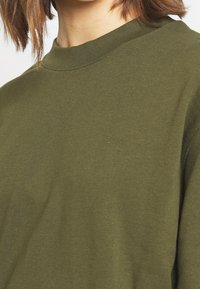 Sudadera de cuello redondo en verde oliva, hecha de material de algodón suave, con un corte holgado y una textura suave, y con cuello acanalado.