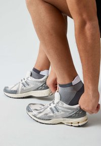 Leichte Laufschuhe in Weiß und Grau mit Mesh-Material, Logo- Akzenten und strukturierten Sohlen. Sichtbarer individuell anpassbarer Socken.