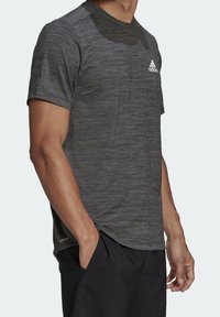Mörkgrå tränings t-shirt i strukturerad tyg, med korta ärmar och ett subtilt randigt mönster. Har en vit logotyp på bröstet.