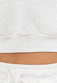 Sweatshirt cropped grigio chiaro con orlo a coste, caratterizzato da una texture di tessuto morbido e una vestibilità rilassata, abbinato a pantaloni della tuta grigio chiaro coordinati.