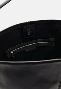 Interior de un bolso tote de cuero negro con una textura suave, un bolsillo con cremallera y un cierre magnético en la parte superior.