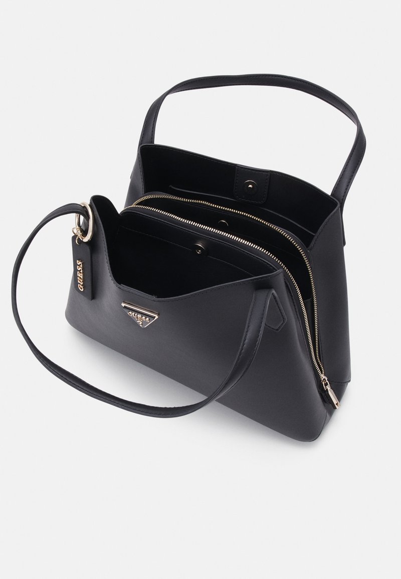 Sac à main en cuir noir avec deux poignées et plusieurs compartiments, un zippé et un à bouton-pression, comportant un logo métallique et une étiquette de marque.
