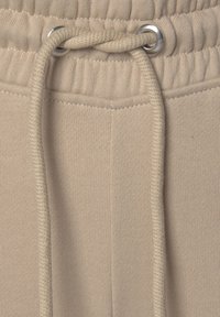 Beige Sweatpants mit einem Kordelzugbund, ausgestattet mit silbernen Ösen, geripptem Bund und einem weichen, strukturierten Stoff.