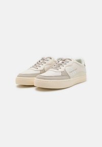 Sneakers in pelle bianca con accenti beige, pannelli laterali testurizzati e lacci piatti. Presentano una punta arrotondata e una suola platform. Logo del marchio sul lato.