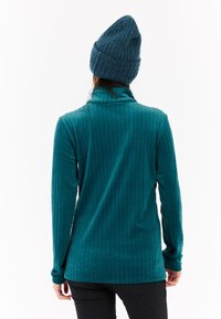 Turkusowa bluzka z długim rękawem i wysokim kołnierzem, wykonana z miękkiego materiału; ma teksturowaną, wzorzystą powierzchnię i jest zestawiona z dopasowaną wełnianą czapką.