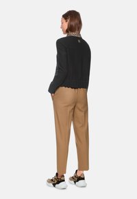 Black jacket with leopard print collar, ribbed hem, paired with beige pants and patterned sneakers. Simple, structured design with contrasting elements.