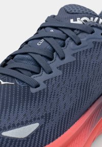 Baskets de sport navy avec une tige en maille texturée, un système de laçage dynamique et une semelle extérieure rembourrée teintée de rouge avec des accents blancs contrastants.