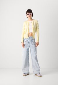 Žltý pletený kardigán s gombíkovým zapínaním, biele crop top, svetlomodré široké nohavice s vreckami vzadu a levanduľové klzáky.
