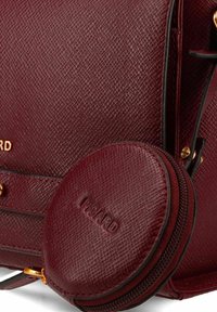 Borsa a mano in pelle borgogna con una finitura testurizzata, dotata di accessori in oro e di una pochette rotonda con zip, con dettaglio del logo impresso visibile.