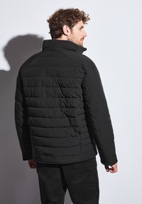 Černá vycpaná bunda s vysokým límcem a horizontálním prošíváním. Hladká textura, přiléhavý střih a jemný lesk.