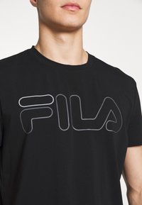 Černé bavlněné tričko s výrazným šedým logem "FILA" v stylizovaném písmu na hrudi, s kulatým výstřihem a krátkými rukávy.