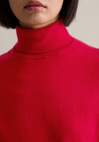 Roter Rollkragenpullover aus weichem Stoff mit einem gerippten Kragen. Nahaufnahme, die sich auf die Textur und die lebendigen Farbdetails konzentriert.