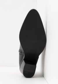 Zapato de cuero negro con punta afilada y tacón bajo de bloque de madera. Textura suave con un detalle mínimo, que presenta un sutil acento de costura.