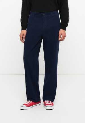 Pantaloni din corduroy bleumarin, cu croială dreaptă, având închidere cu nasture în față și buzunare laterale. Asortați cu adidași roșii din pânză.