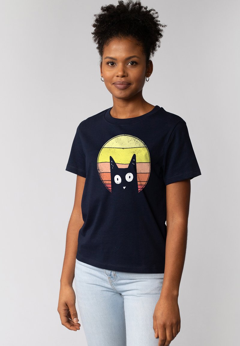 Marineblauwe katoenen t-shirt met een grafisch ontwerp van een zwarte kat met grote witte ogen, tegen een ronde zonsondergangsgradient van gele en oranje strepen.