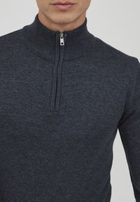 Mørk grå zip-up genser med høy krage, laget av myk strikket stoff. Har en sølvfarget glidelås og en tettsittende design.