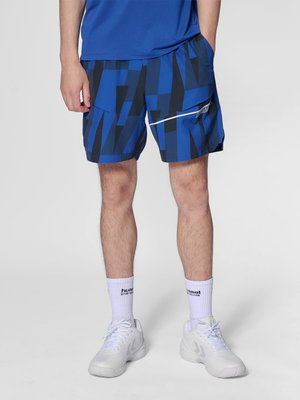 Man draagt blauwe en zwarte korte broek met geometrisch patroon, witte sportschoenen en witte sokken met zwarte letters.