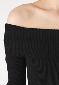 Svart av-hulenn ribbet topp med lange ermer, med et teksturert strikkemønster og en glatt, tettsittende design.