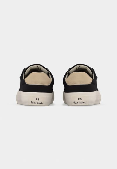 Paire de baskets basses noires avec des languettes de talon beige et des semelles blanches, vues de dos, arborant le logo « PS Paul Smith » sur les talons.