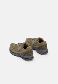Chaussures de course en mesh vert olive avec une surface texturée, un laçage à l'avant et une semelle en caoutchouc grise comportant plusieurs sections amortissantes.