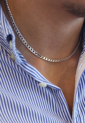 Collier en chaîne argenté avec des maillons entrelacés, affichant une texture lisse. Positionné contre une chemise à rayures bleues et blanches.