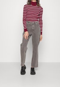 Pull en col roulé rayé maroon et blanc, associé à un jean large taille haute gris et des mocassins à plateformes noirs.